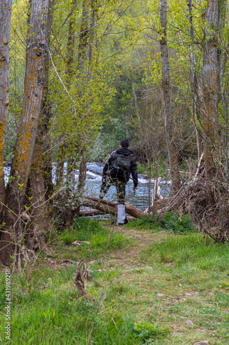 Teenager with fishing suit, rod and tools crossing some branches of the trees to go to the river to catch trout and other fish to enjoy an afternoon