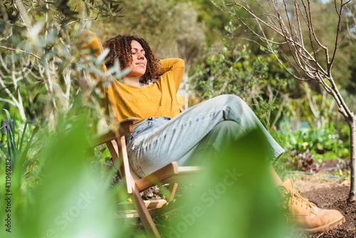 Woman with hands behind head relaxing on deck chair in garden photo