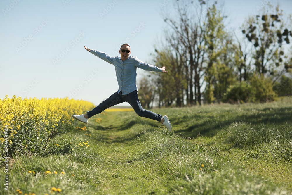 A young man in sunglasses is walking and having fun through a Sunny yellow rapeseed field, the concept of travel and freedom. summer holiday background