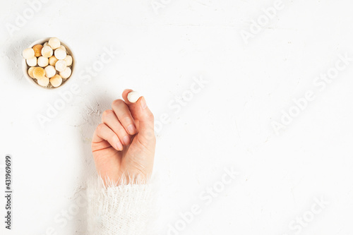 The hand of a young girl in a white fluffy sweater holds a traditional asian cheese kurut next to a plate of dry round cheese on a white background copy space photo
