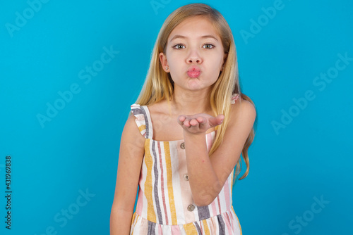 Fotografi beautiful Caucasian little girl wearing stripped dress over blue background looking at the camera blowing a kiss with hand on air being lovely and sexy