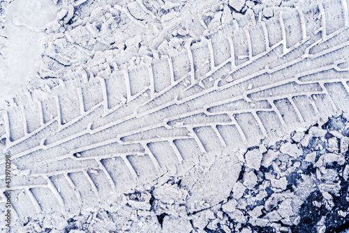 Diagonal traces of car tires in the snow on the asphalt. Close up view from above
