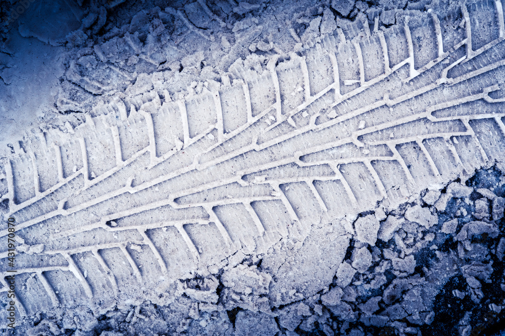 Fototapeta premium Diagonal traces of car tires in the snow on the asphalt. Close up view from above