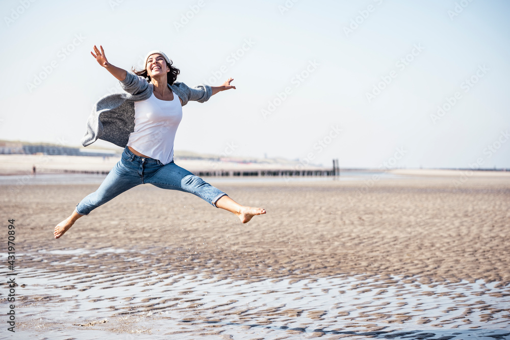Cheerful young woman jumping over wet sand on sunny day Cheerful young woman jumping over wet sand on sunny day
