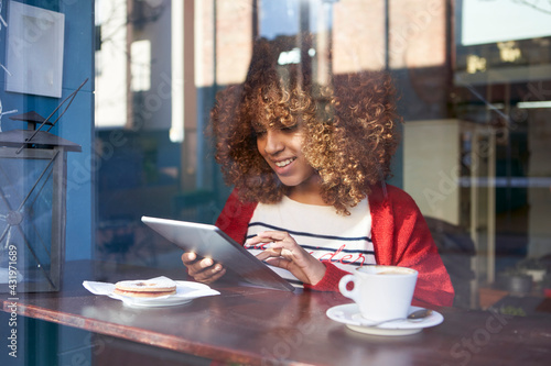 Smiling Afro woman using digital tablet while sitting at cafe photo
