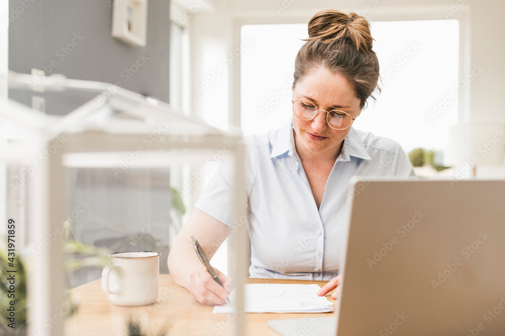 Businesswoman sitting at desk writing on document Businesswoman sitting at desk writing on document