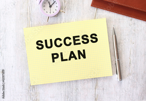 SUCCESS PLAN text written in a notebook lying on a wooden work table.
