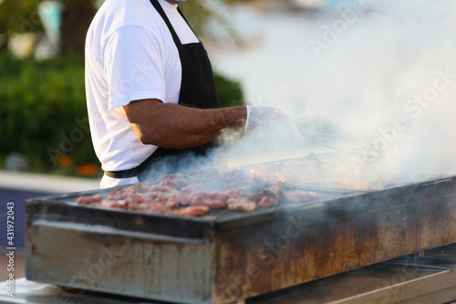 Cook prepares meat on grill on street