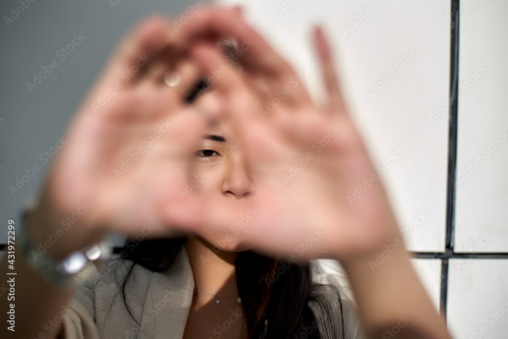 Young woman against wall while looking through hand Young woman against wall while looking through hand