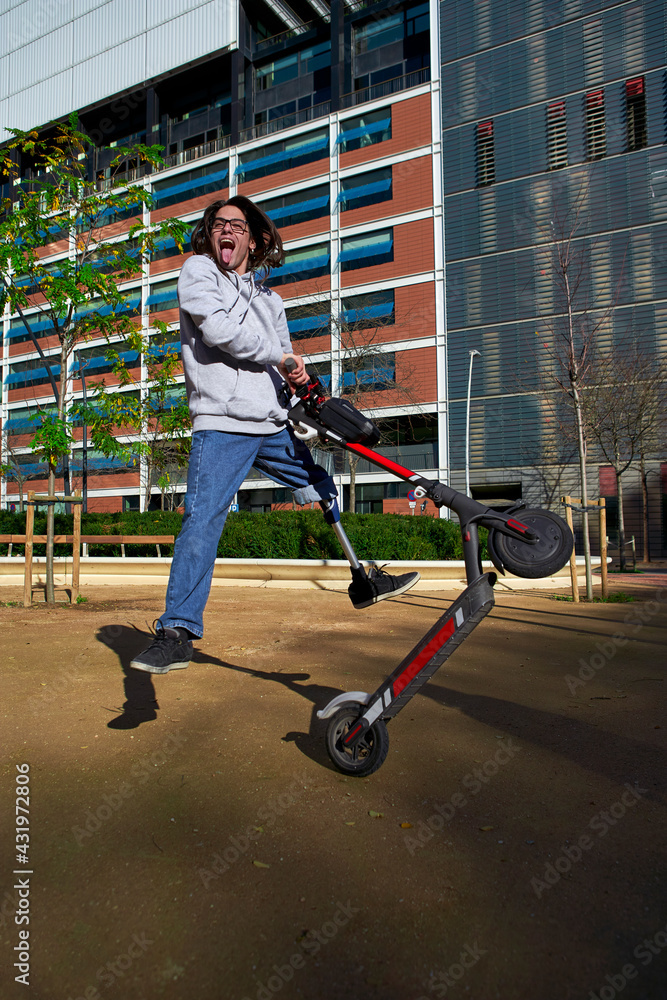 Cheerful young disabled man practicing stunt on electric push scooter in playground against buildings Cheerful young disabled man practicing stunt on electric push scooter in playground against buildings