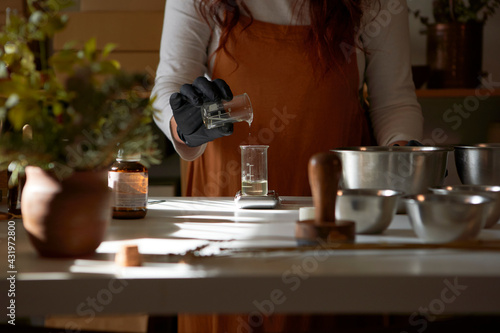 Woman pouring ingredient in glass beaker while making soap in workshop photo