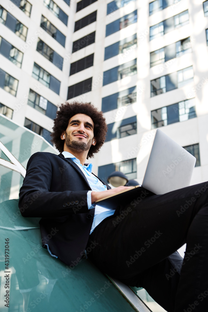 Smiling male entrepreneur with laptop leaning on glass wall against building Smiling male entrepreneur with laptop leaning on glass wall against building