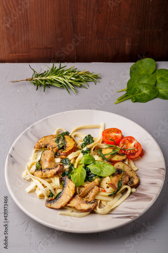 Udon with mushrooms and spinach and cherry tomatoes in a plate next to greens.