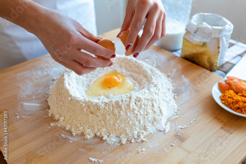 Woman breaking egg in flour on cutting board in kitchen photo