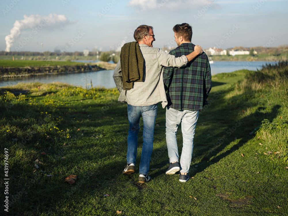 Father arm around son walking at riverbank Father arm around son walking at riverbank
