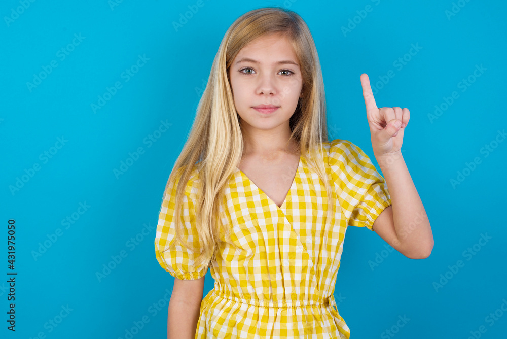beautiful Caucasian little girl wearing yellow dress over blue background smiling and looking friendly, showing number one or first with hand forward, counting down beautiful Caucasian little girl wearing yellow dress over blue background smiling and looking friendly, showing number one or first with hand forward, counting down