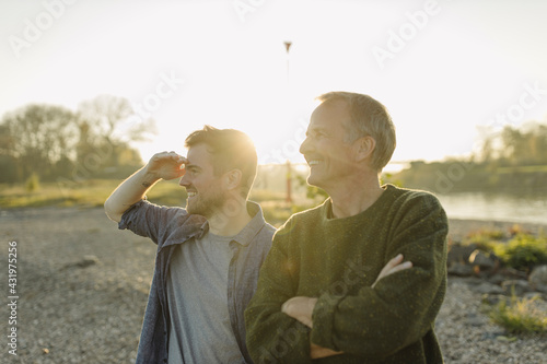 Smiling son searching while standing by father on riverbank at evening photo