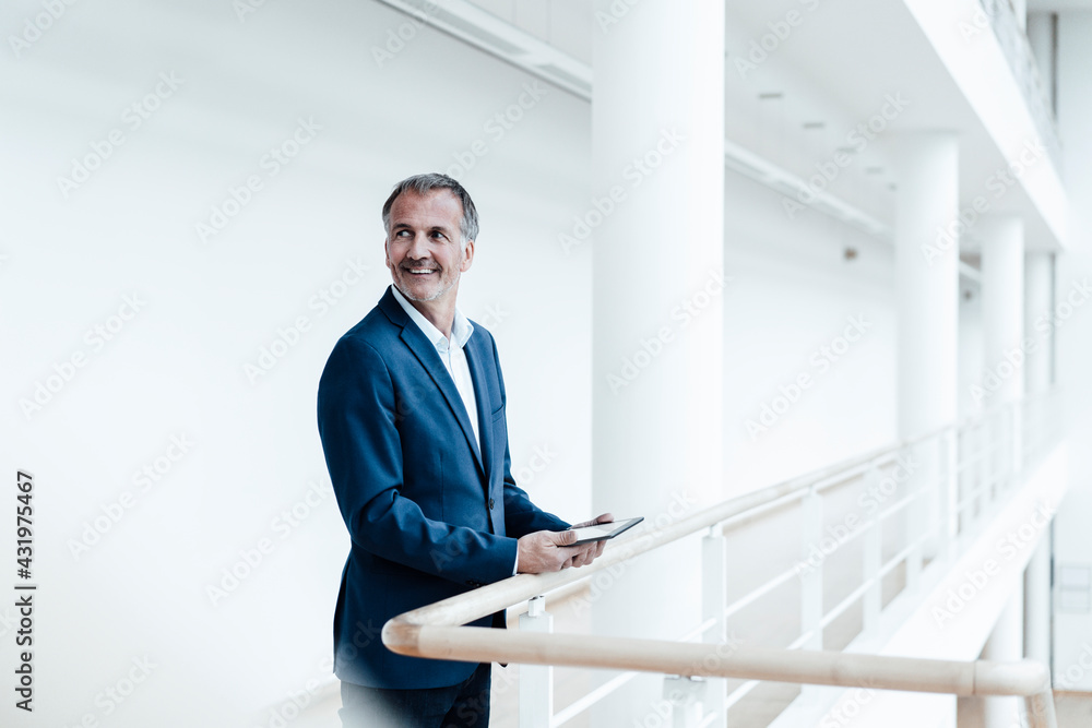 © Gustafsson/Westend61 - Smiling male business professional holding digital tablet at railing in office corridor © Gustafsson/Westend61 - Smiling male business professional holding digital tablet at railing in office corridor