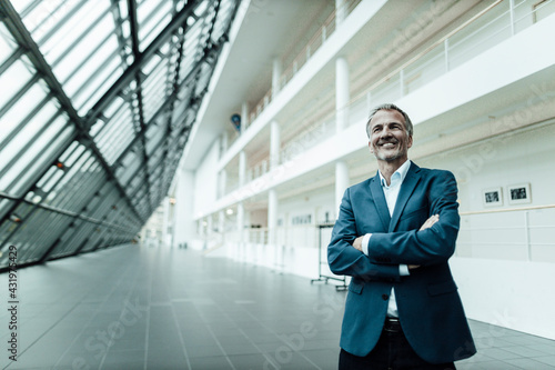 Wallpaper Mural Smiling businessman with arms crossed looking away while standing in office corridor Torontodigital.ca