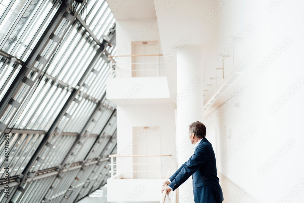 Senior businessman leaning on railing in corridor at office Senior businessman leaning on railing in corridor at office