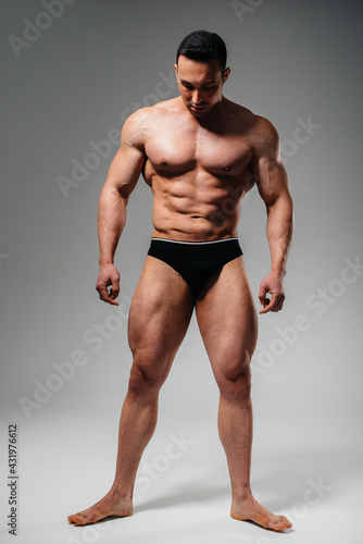 A young athlete bodybuilder poses in the studio topless, showing off his abs and muscles. Sport.