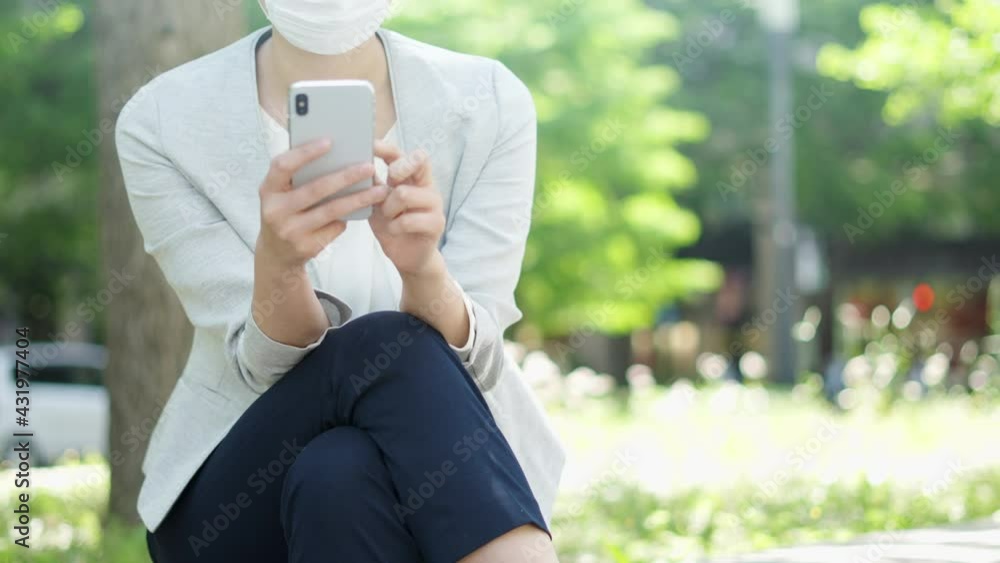 屋外でスマートフォンを操作するマスク姿のビジネスウーマン 屋外でスマートフォンを操作するマスク姿のビジネスウーマン