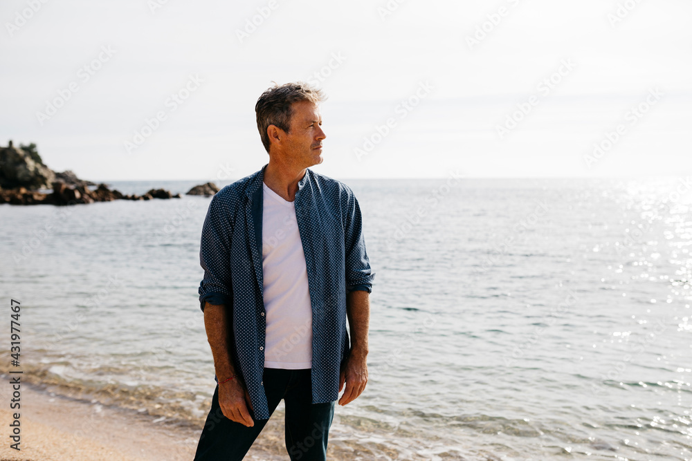 Mature man looking away while standing against sea on beach Mature man looking away while standing against sea on beach