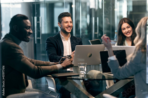 Smiling colleague looking at businesswoman while sitting in meeting at office