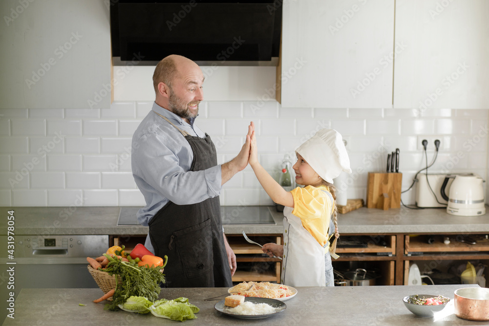Mature men and girl cheering with giving high-five while standing in kitchen at home Mature men and girl cheering with giving high-five while standing in kitchen at home