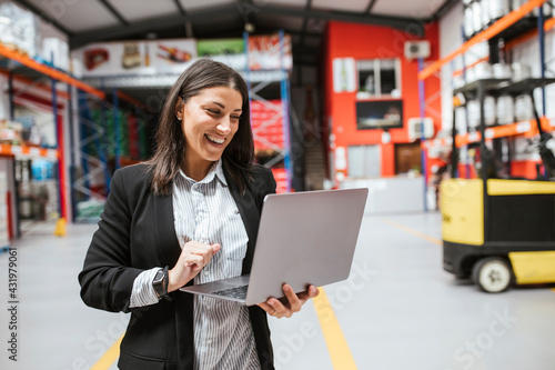 Smiling female manager using laptop in illuminated distribution warehouse photo