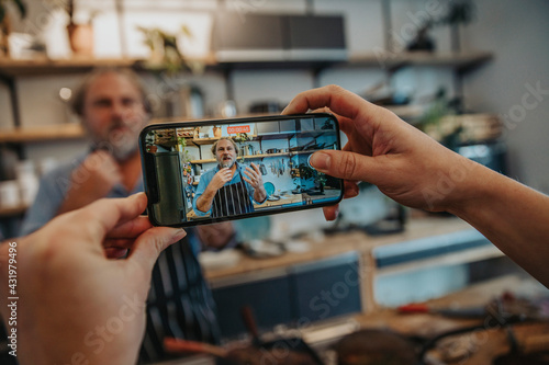 Woman filming chef through mobile phone while standing in kitchen photo
