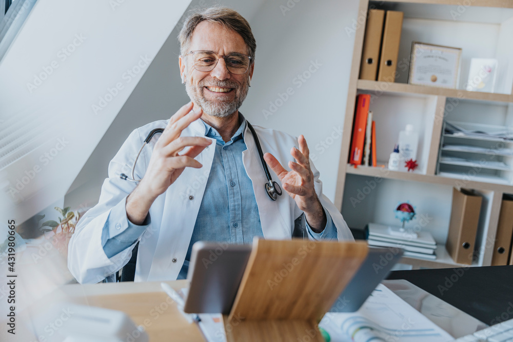 © Mareen Fischinger/Westend61 - Male doctor gesturing while talking on video call over digital tablet at doctor's office © Mareen Fischinger/Westend61 - Male doctor gesturing while talking on video call over digital tablet at doctor's office