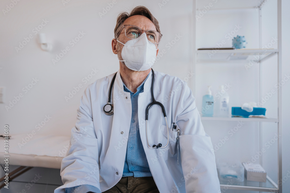 Thoughtful doctor with protective face mask looking away while sitting in clinic Thoughtful doctor with protective face mask looking away while sitting in clinic