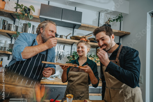 Male chefs tasting salami while standing by colleague in kitchen photo