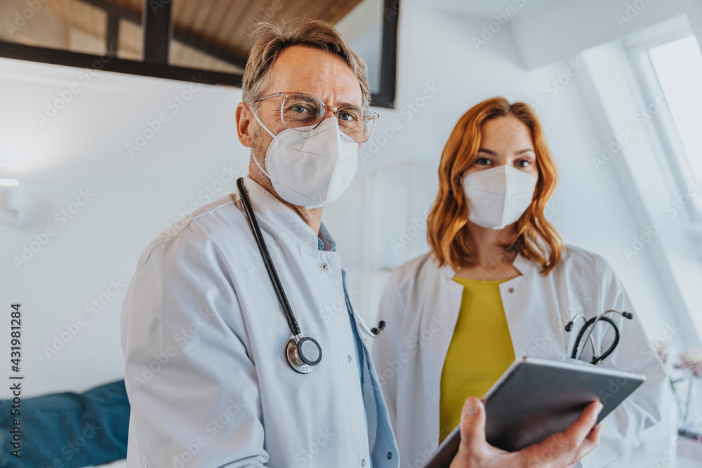 Male doctor with digital tablet standing by coworker in clinic Male doctor with digital tablet standing by coworker in clinic