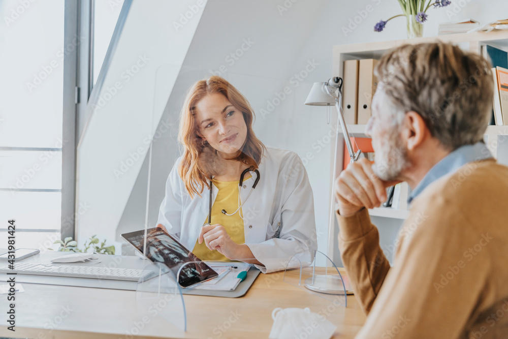 Female doctor explaining patient over x-ray while sitting by screen partition at doctor's office Female doctor explaining patient over x-ray while sitting by screen partition at doctor's office