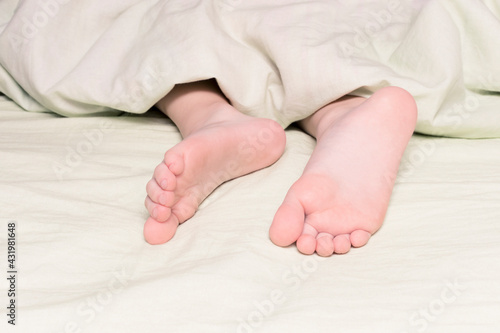 Legs sticking out from under the blanket close-up. The concept of sleep, insomnia or sound sleep, lullaby