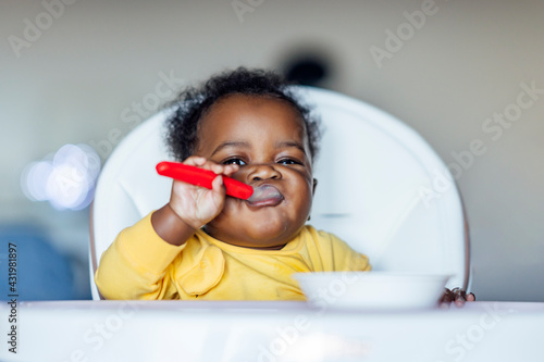 Baby girl eating with spoon while sitting on high chair at home photo