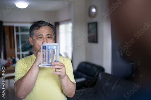 Old man uses a Tri-ball Incentive Spirometer for check his lung function.