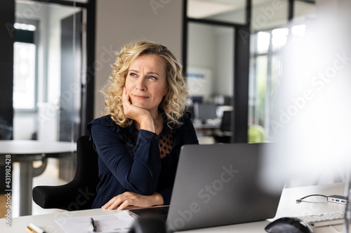 Thoughtful female business professional with head in hand looking away while sitting at desk in office photo