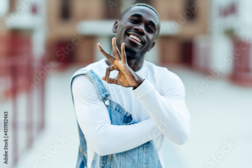 Smiling young man in denim bib overalls gesturing OK sign