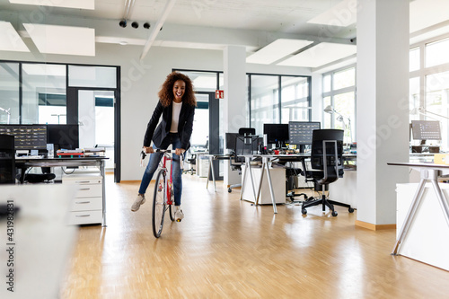 Cheerful businesswoman riding bicycle in open plan office photo
