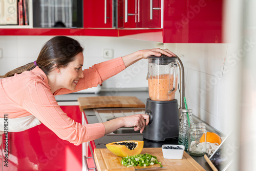 Woman using blender to prepare smoothie in kitchen at home