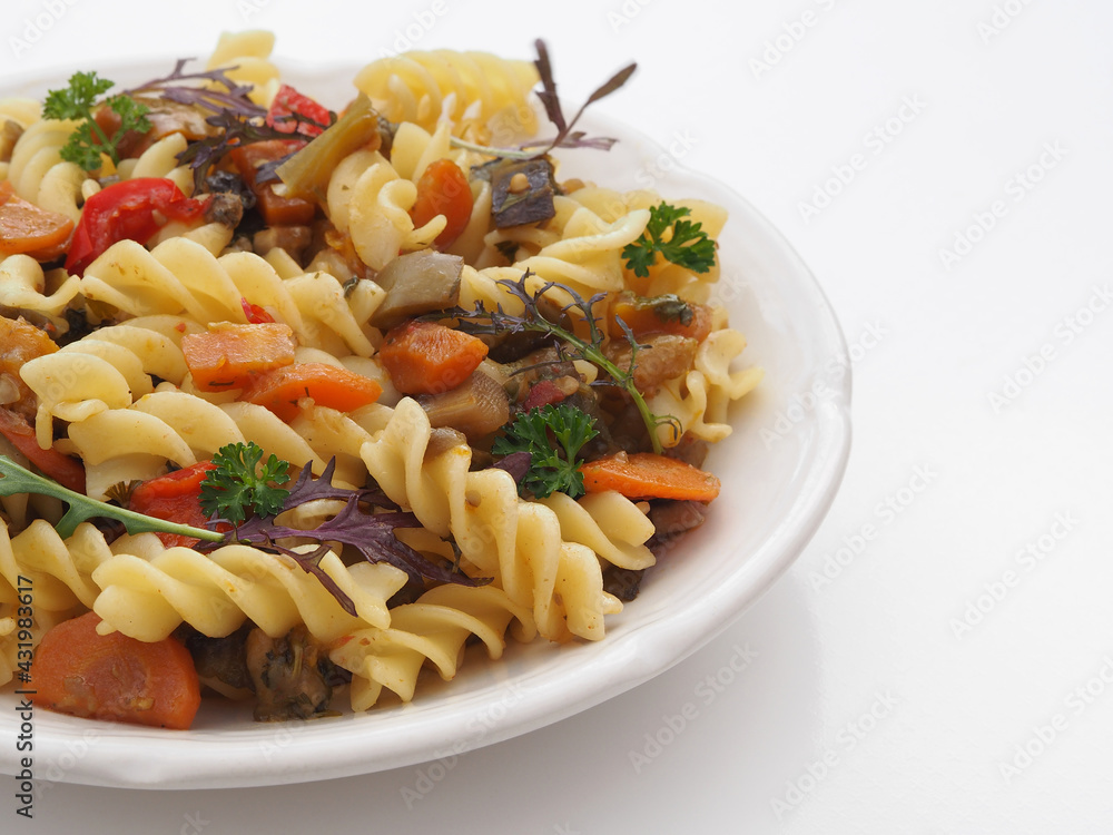 Pasta with a sauce of different vegetables and herbs in a plate on a white background, top view, copy space. Healthy dish with curly macaroni and stewed vegetables for a proper vegetarian diet Pasta with a sauce of different vegetables and herbs in a plate on a white background, top view, copy space. Healthy dish with curly macaroni and stewed vegetables for a proper vegetarian diet