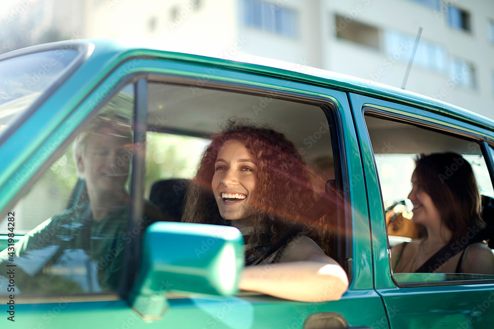 © LOUIS CHRISTIAN/Westend61 - Smiling woman looking away while sitting with friends in car