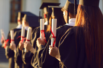 Selective focus on diverse graduation student in academic cap and gown hold diploma in commencement ceremony row. Graduate.Education accomplishment and high degree achievement party celebration