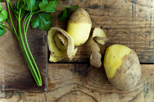 Half peeled potatoes and parsley leaves on rustic wooden background