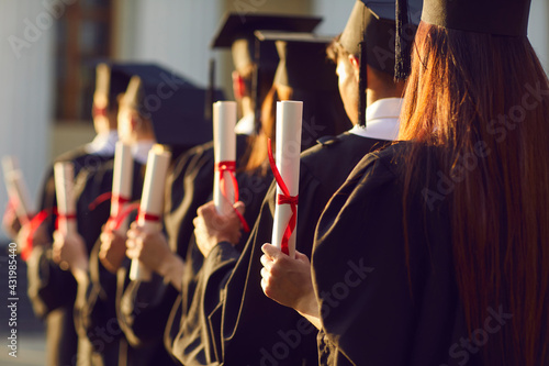 Selective focus on diverse graduation student in academic cap and gown hold diploma in commencement ceremony row. Graduate.Education accomplishment and high degree achievement party celebration