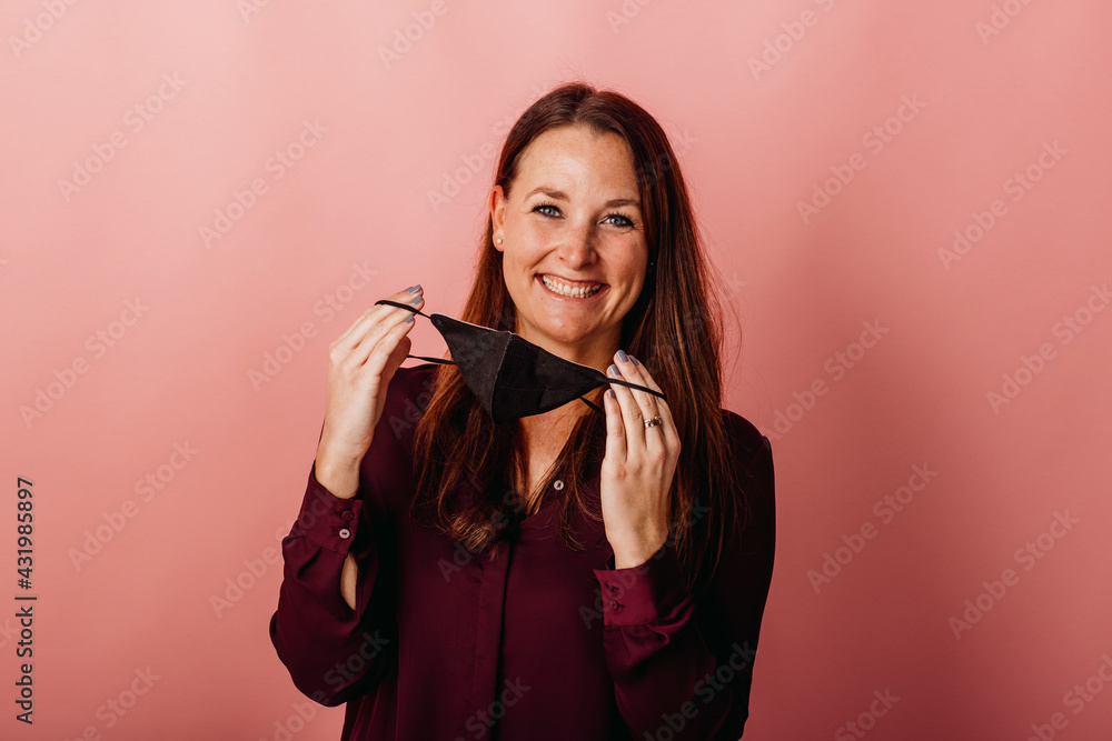 Smiling businesswoman holding protective face mask while standing against colored background Smiling businesswoman holding protective face mask while standing against colored background