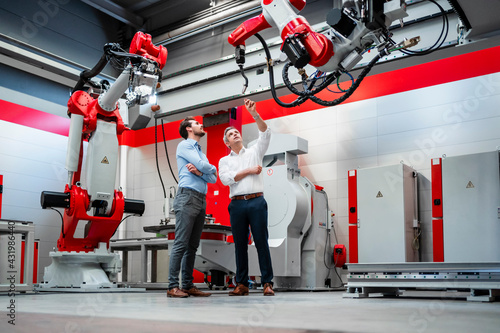 Male engineer explaining robotic arm to colleague in factory photo